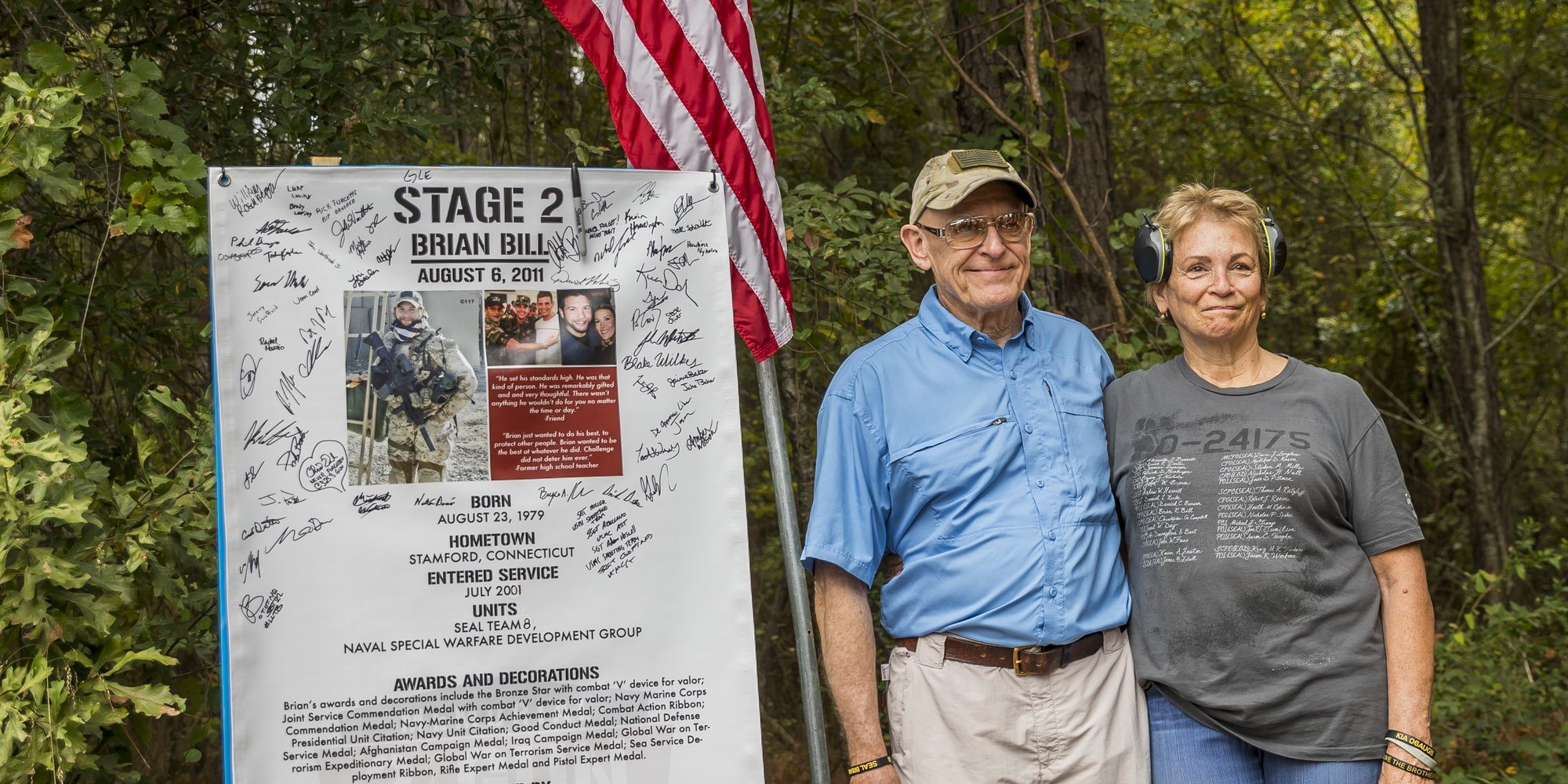 A Gold Star mother and father gather at their son's signed stage sign and the American flag at the 2023 Memorial 3 Gun