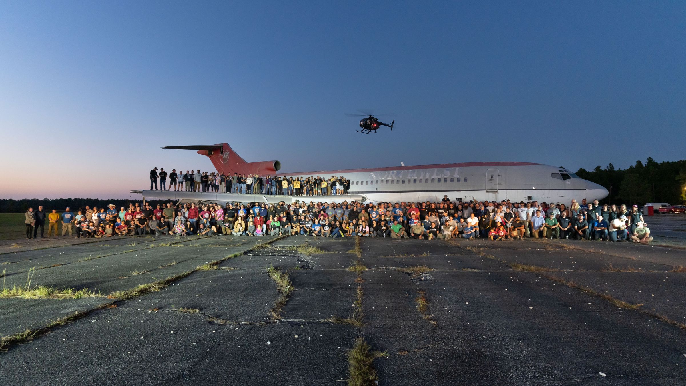 Competitors and families gather for a Memorial 3 Gun group photo by a helicopter
