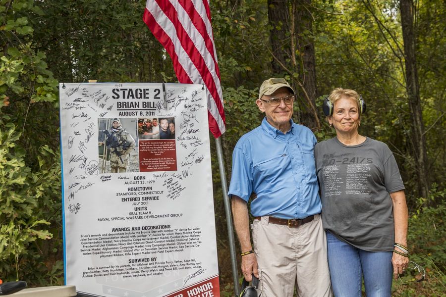 Patricia Parry and Dr. Michael Parry, mother and stepfather of SOC (SEAL) Brian R. Bill, beside his signed Stage 2 sign at the 2023 Memorial 3 Gun