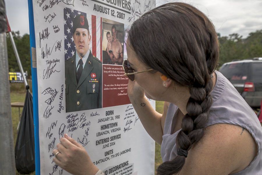 A woman rests her hand on the signed stage sign for SSG Jesse Clowers at the 2023 Memorial 3 Gun