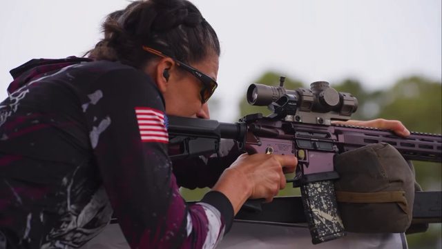 A Memorial 3 Gun competitor sights in her rifle on a stage
